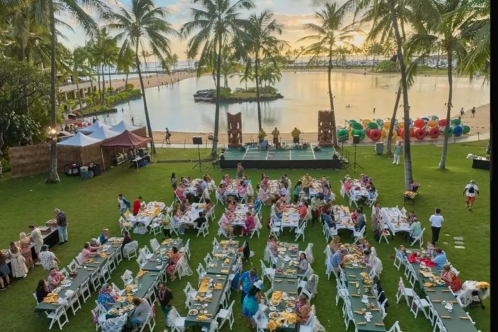 People dining at an outdoor event near a beach with palm trees and sunset.