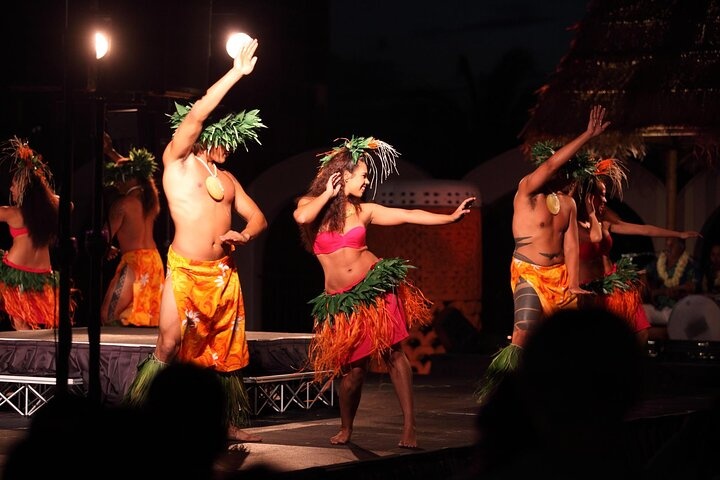 Dancers in grass skirts and headdresses perform a traditional dance on stage.